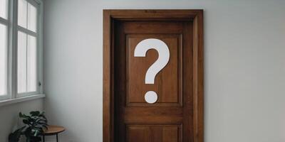 A wooden door with a question mark on it is in a room with a white wall. photo