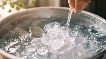 A hand stirring a tub of ice water and essential oils creating a mix of scents and benefits for a refreshing and rejuvenating bath photo