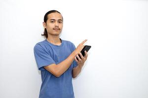 Asian man wearing dark blue t-shirt holding smartphone, very happy while pointing with hand and finger to the side. isolated in white background photo