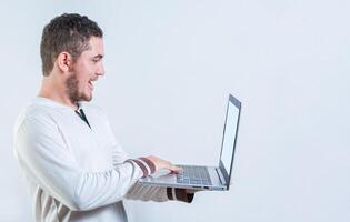 Portrait of happy young man standing using laptop isolated. Excited guy holding and looking at an promotion on laptop screen photo