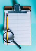 Notepad with pencil and magnifying glass on isolated background. Note book with magnifying glass and pencil on clipboard photo