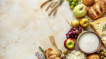 Shabbat food on a white table, including bread, cheese, apples, grapes, and a bowl of milk or water, against a light background with space for text. photo