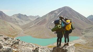 Two caucasian adult hikers together stand hugging caring on top mountain enjoy panorama. Man and woman standing and hugging on the top of the mountain, autumn hike with backpacks.Alpine Kelitsadi lake video