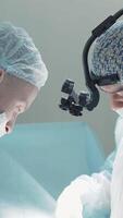 Two surgeons busy at work . Action . Two men in blue lab coats are painstakingly working on a complex operation , using various medical accessories like microscopic glasses video
