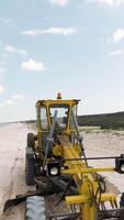 Yellow tractor. Shot . A large tractor working on the ocean shore, which drives at speed and rakes heaps of sand and the blue sky is visible. video