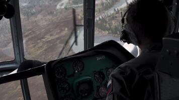 The view from the helicopter. Clip. The pilot controls the helicopter over a large green forest in calm weather . video