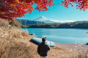 man tourist with Fuji Mountain at Lake Saiko in Autumn season, happy Traveler travel Mount Fuji, Yamanashi, Japan. Landmark for tourists attraction. Japan Travel, Destination and Vacation photo