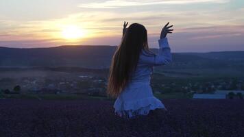 Woman with long hair in white dress dances joyfully in lavender field at sunset, happy and blissful moment. Lush lavender bushes in endless rows. Garden aromatherapy. Slow motion video