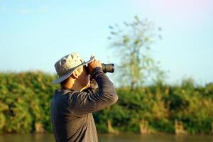Asian man uses binoculars to observe local birds along a river. Soft and selective focus photo