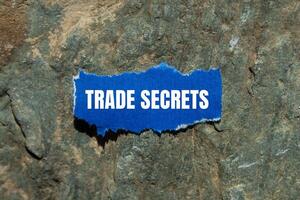 Trade secrets message written on ripped torn blue paper piece with stone background. Conceptual trade secrets symbol. Copy space. photo