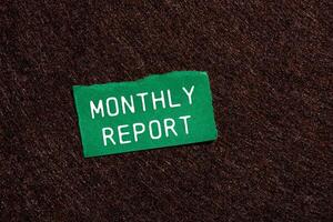 Monthly report message written on ripped torn green paper piece on brown background. Conceptual monthly report symbol. Copy space. photo