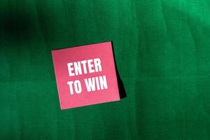 Enter to win message written on pink paper with green background. Conceptual enter to win symbol. Copy space. photo
