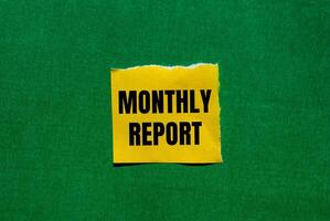 Monthly report message written on ripped torn yellow paper piece on green background. Conceptual monthly report symbol. Copy space. photo