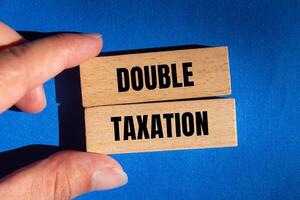 Double taxation message written on wooden blocks with blue background. Conceptual double taxation symbol. Copy space. photo