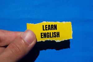 Learn english message written on ripped torn yellow paper with blue background. Conceptual learn english symbol. Copy space. photo