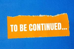 To be continued message written on ripped torn orange paper with blue background. Conceptual to be continued symbol. Copy space. photo