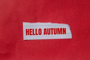 Hello autumn message written on ripped torn paper piece with red background. Conceptual hello autumn symbol. Copy space. photo