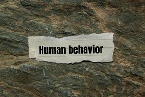 Human behavior message written on ripped torn paper piece on stone background. Conceptual human behavior symbol. Copy space. photo