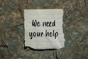 We need your help message written on ripped torn paper piece on stone background. Conceptual we need your help symbol. Copy space. photo