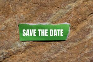 Save the date message written on ripped torn green paper piece with stone background. Conceptual save the date symbol. Copy space. photo