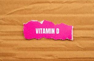 Vitamin d message written on ripped pink torn paper piece with cardboard background. Conceptual vitamin d symbol. Copy space. photo