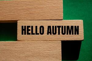 Hello autumn message written on wooden blocks with green background. Conceptual hello autumn symbol. Copy space. photo