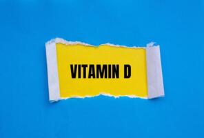 Vitamin d message written on ripped torn blue paper with yellow background. Conceptual vitamin d symbol. Copy space. photo
