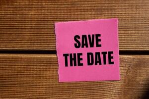 Save the date message written on ripped torn pink paper piece with wooden background. Conceptual save the date symbol. Copy space. photo