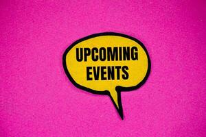 Upcoming events message written on yellow paper speech bubble with pink background. Conceptual upcoming events symbol. Copy space. photo