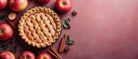 Freshly Baked Apple Pie with Lattice Crust Surrounded by Red Apples and Cinnamon Sticks on a Pink Background photo