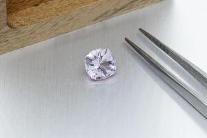 macro mineral faceted stone Morganite with tweezers on a gray background photo