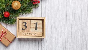 christmas tree branch with toys and gifts and wooden calendar december 31 on a wooden background photo