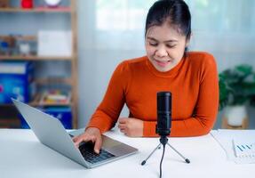 Woman talking into microphone on stand, lead on-line communication, discuss topic, looks at notebook screen, engaged in streaming, virtual meeting event, Podcast, webinar, Content creator concept. photo