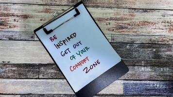 Concept of Be Inspired Get Out Of Your Comfort Zone write on paperwork isolated on wooden background. photo