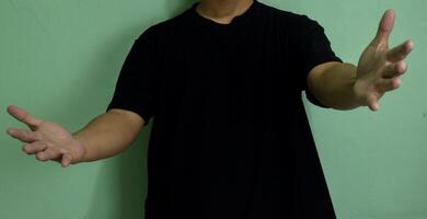 Young man greeting and hugging over on green background. Showing welcome gesture and holding empty raise hands photo
