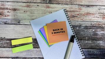 Concept of Back in 5 Minutes write on sticky notes isolated on Wooden Table. photo
