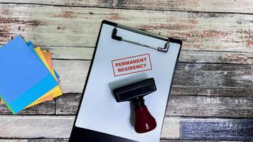 Red Handle Rubber Stamper and Permanent Residency text on a paperwork isolated on wooden background photo