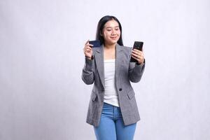 beautiful young woman office smile hold mobile phone smartphone and hold credit debit member card wearing grey suit isolated on white background. for communication, finance, transaction content photo