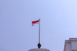 An Indonesian red and white flag flies above a colonial architectural building photo