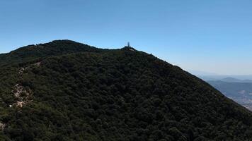 A serene hilltop view of lush green mountains and a distant structure under a bright blue sky during midday video