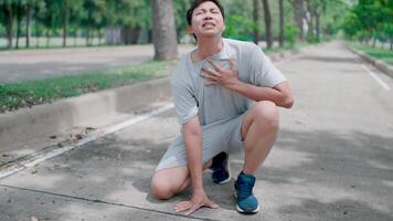 Asian tan man feel exhausted and tiredpain heart attack while exercise in park. Attractive sportsman has difficulty breath clutching chest from acute pain while practice workout for health in park. video