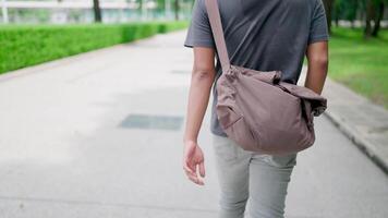 Behind, Man is walking with his hands in his pants and holding a laptop in the park, working online, He is walking in nature to relax from work and study, studying online, modern tech concept. video