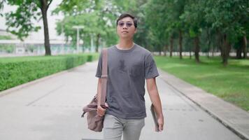 Male student walking with laptop and bag in the park, working online, He is walking in nature to relax from work and study, studying online, modern tech concept. video