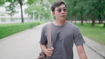 Nahansicht männlich Schüler Gehen mit Laptop und Tasche im das Park, Arbeiten online, er ist Gehen im Natur zu entspannen von Arbeit und lernen, studieren online, modern Technik Konzept. video