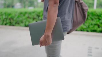 Close-up Male student walking with laptop and bag in the park, working online, He is walking in nature to relax from work and study, studying online, modern tech concept. video