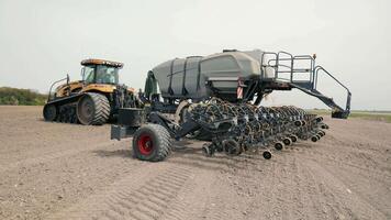 Large tractor with attached seed drill in a field, A large yellow tractor equipped with a seed drill attachment is parked in an open field, ready for agricultural planting video