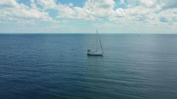 Sailboat floating in the middle of the ocean on a calm day. A peaceful scene of a lone sailboat floating in the vast ocean on a calm day. video