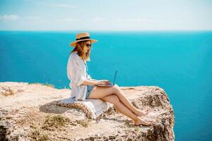 Freelance woman working on a laptop by the sea, typing away on the keyboard while enjoying the beautiful view, highlighting the idea of remote work. photo