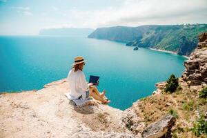 Freelance woman working on a laptop by the sea, typing away on the keyboard while enjoying the beautiful view, highlighting the idea of remote work. photo