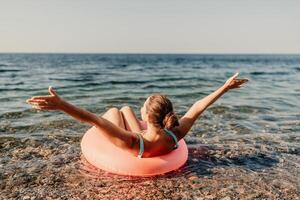 A woman is floating on a pink inflatable raft in the ocean. She is smiling and she is enjoying herself. photo